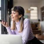 Young woman sending audio message on smartphone at home